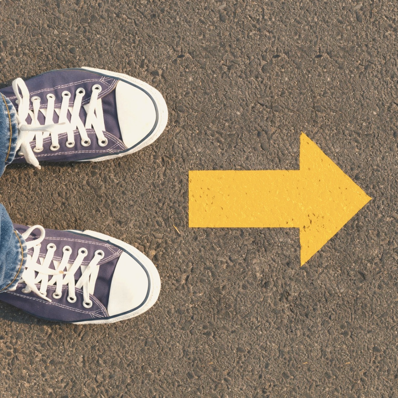 Purple sneakers on asphalt beside a honey-gold arrow pointing forward — a reminder that growth begins with one intentional step