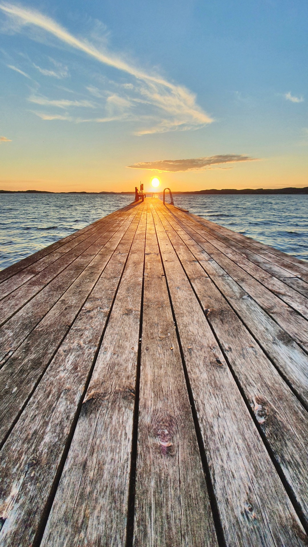 A wooden pier reaching over calm water toward a bright sunset horizon